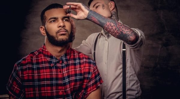 old-fashioned-professional-tattooed-hairdresser-does-haircut-african-american-client-using-scissors-comb-isolated-dark-textured-background_613910-19483