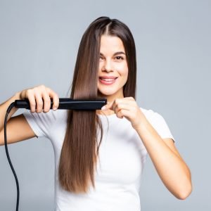 Smiling woman straightening her hair with white background