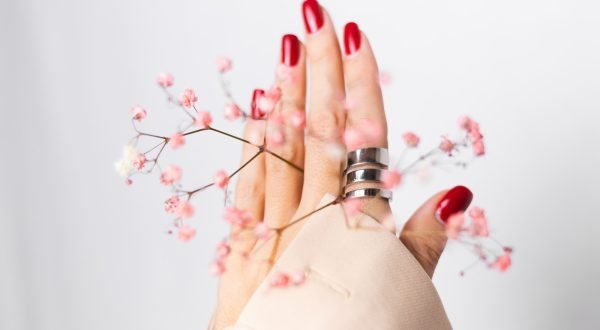 soft-gentle-photo-woman-hand-with-big-ring-red-manicure-hold-cute-little-pink-dried-flowers-white